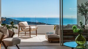 A modern living room with a large glass window, a sofa, a chair, and a small table with a vase. - Palo Alto Marbella Luxury Apartment – Sea View, Wi-Fi & Air Conditioning (Ojén)