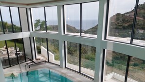 An indoor swimming pool with large windows offering views of a hilly landscape. - Palo Alto Marbella Luxury Apartment – Sea View, Wi-Fi & Air Conditioning (Ojén)