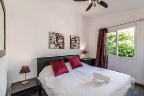 A bedroom with a bed, two nightstands, a ceiling fan, and artwork on the wall.
