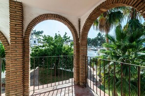 Un balcon orné d’arches en briques, doté d’une balustrade en métal, et offrant une vue sur la verdure et les bâtiments.