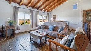 A cozy living room with a wooden ceiling, a sofa, a coffee table, and a fireplace. - Holiday Home 'Casa Andrea' with Mountain Views, Shared Pool & Wi-Fi (Barbate)