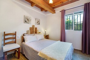 Un dormitorio con una cama, una silla de madera, una mesita de noche y una ventana con cortinas.
