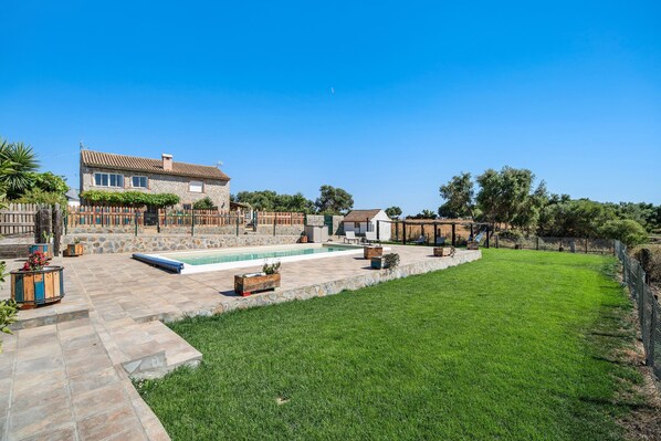 Un patio trasero con piscina, patio de piedra y una casa de fachada de piedra.