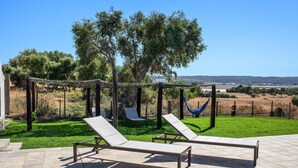 A patio with two lounge chairs, a hammock, and a pergola with vines. - Holiday Home 'Casa Andrea' with Mountain Views, Shared Pool & Wi-Fi (Barbate)