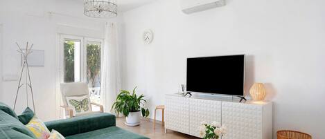 Una sala de estar con un sofá verde, un armario blanco, un televisor de pantalla plana, una planta en maceta y una cesta de mimbre.
