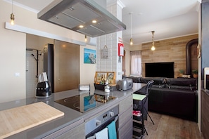 A modern kitchen with a built-in stove, a toaster, and a coffee maker. There is a dining area with a black sofa and a TV.