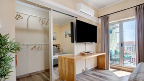 Een hotelkamer met een schuifdeur, een flatscreen televisie, een houten bureau, een balkon met uitzicht en een plant.