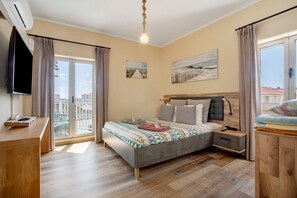 Un dormitorio con cama, mesitas de noche, televisor y vista al balcón.