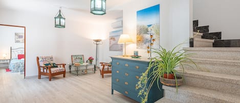A spacious living area with a staircase, a blue dresser, a chair, a lamp, and a painting.