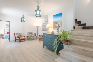 Un amplio salón con una escalera, un aparador azul, una silla, una lámpara y un cuadro.
