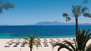 A beach with umbrellas and lounge chairs, a clear view of the sea, and mountains in the distance. - Vacation Home 'Tanamar' near Beach with Balcony & Wi-Fi (Puerto Pollensa)