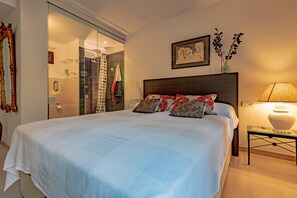 A bedroom with a large bed, a bedside table with a lamp, a picture on the wall, and a door leading to a bathroom. - 'Apartment Rafael' with Sea View, Terrace & Wi-Fi (Port de Pollença)
