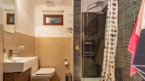 A bathroom with a sink, toilet, shower, and a mirror.