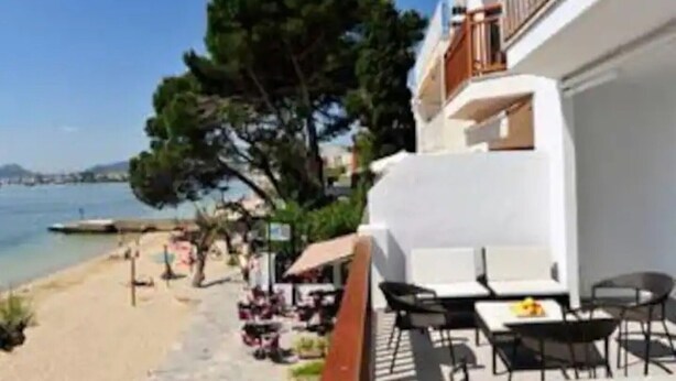 A seaside hotel with outdoor seating, a view of the beach, and a clear sky.