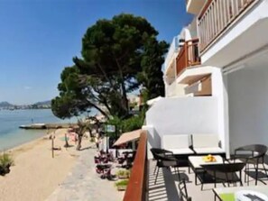 A seaside hotel with outdoor seating, a view of the beach, and a clear sky.
