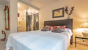 A modern bedroom with a large bed, a bedside table with a lamp, a mirror, and a framed picture on the wall.