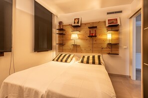 A bedroom with a bed, bedside lamps, a wooden headboard with shelves, and a door to the right. - 'Apartment Rafael' with Sea View, Terrace & Wi-Fi (Port de Pollença)