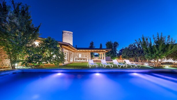Una piscina con sillones reclinables, una torre de piedra y un patio cubierto.