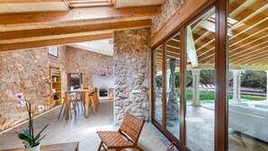 Una habitación amplia con paredes de piedra, vigas de madera, un gran ventanal y un comedor con sillas y una mesa.