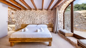 Un dormitorio con pared de piedra, vigas de madera, cama y ventana con vistas.
