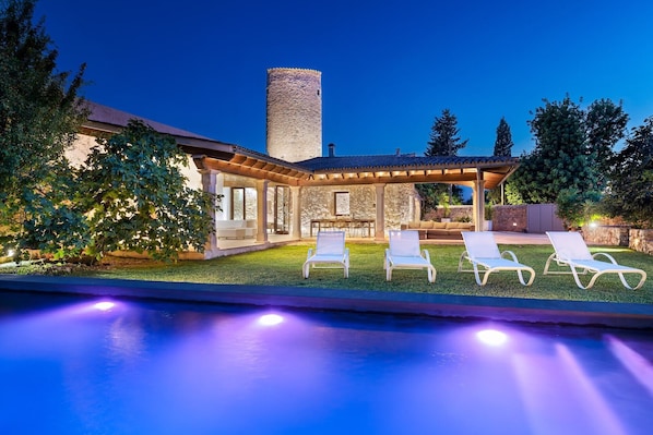 A poolside area with lounge chairs, a stone building, and a tower.