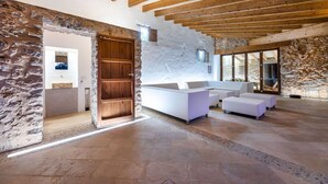 Una habitación amplia con pared de piedra, vigas de madera en el techo y un conjunto de sofá blanco.