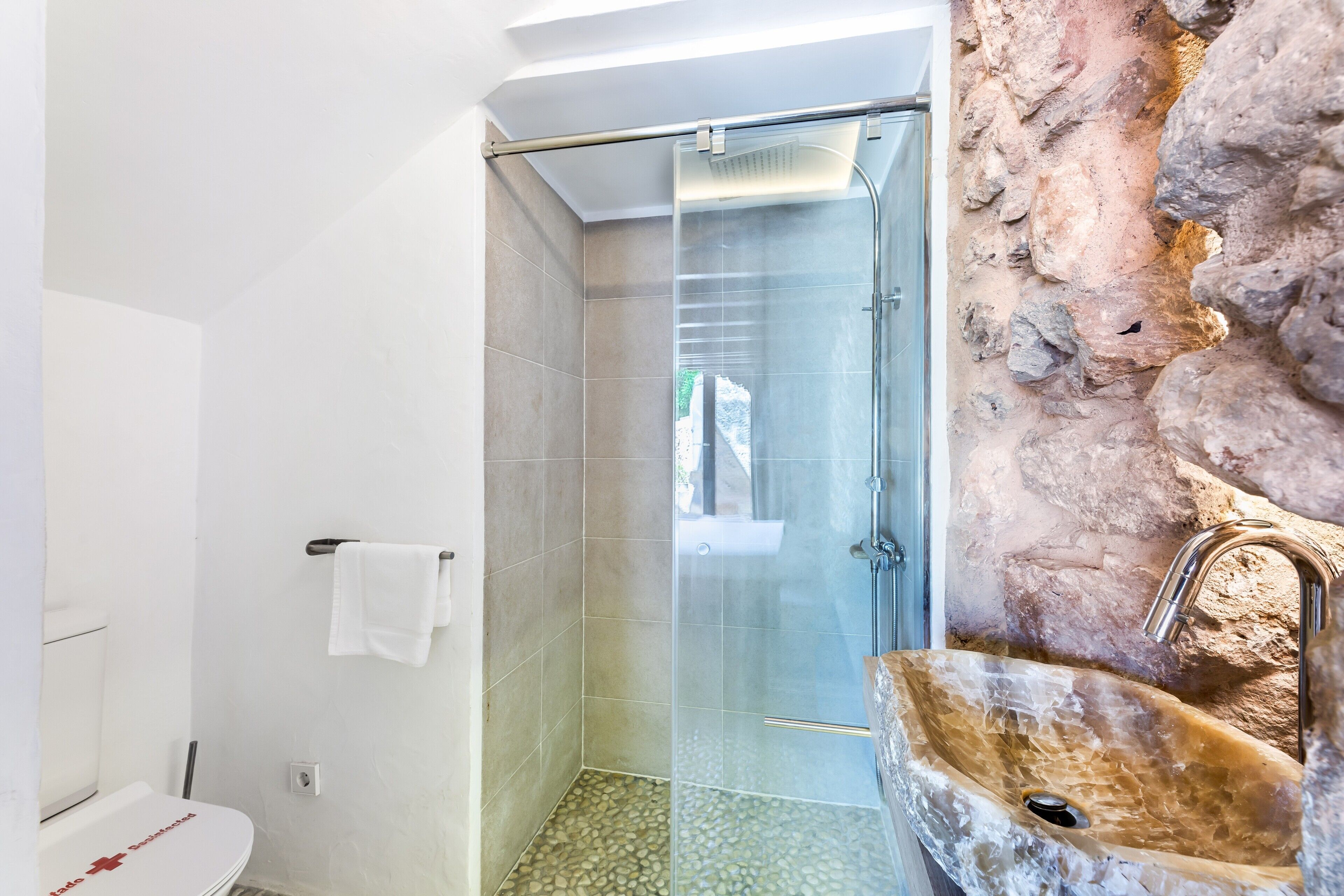 Un baño con cabina de ducha de vidrio, lavamanos de piedra y una toalla blanca colgada en un perchero.