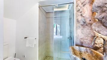 Un baño con cabina de ducha de vidrio, lavamanos de piedra y una toalla blanca colgada en un perchero.