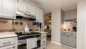 Una cocina con muebles blancos, estufa de acero inoxidable y una zona para café.