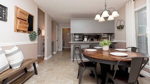 Una cocina moderna con una isla central, un comedor con una mesa redonda y sillas, y un banco con cojines.