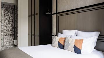 A neatly made bed with white and patterned pillows, a dark headboard, and a wall with a geometric design.