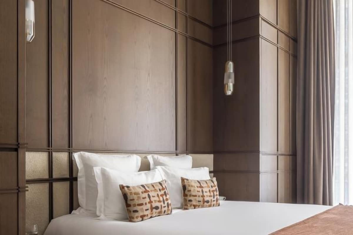 A hotel room with a large bed, a wooden headboard, and a hanging light fixture.