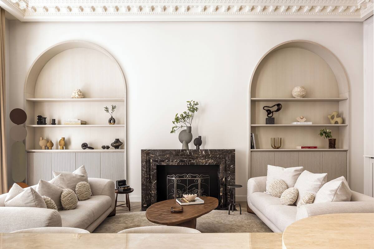 A living room with two sofas, a coffee table, and a fireplace. Shelves with decorative items are on either side of the fireplace.
