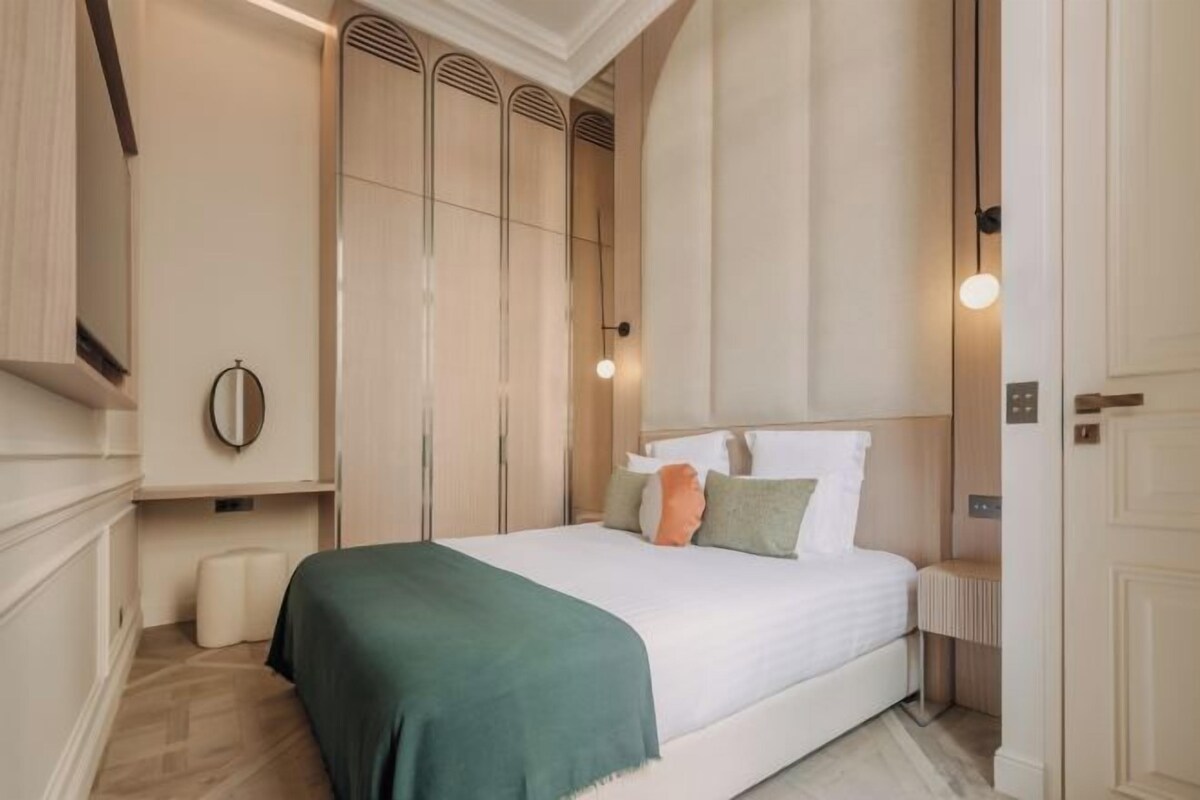 A bedroom with a large bed, a bedside table, a mirror, and a wardrobe with built-in ventilation.