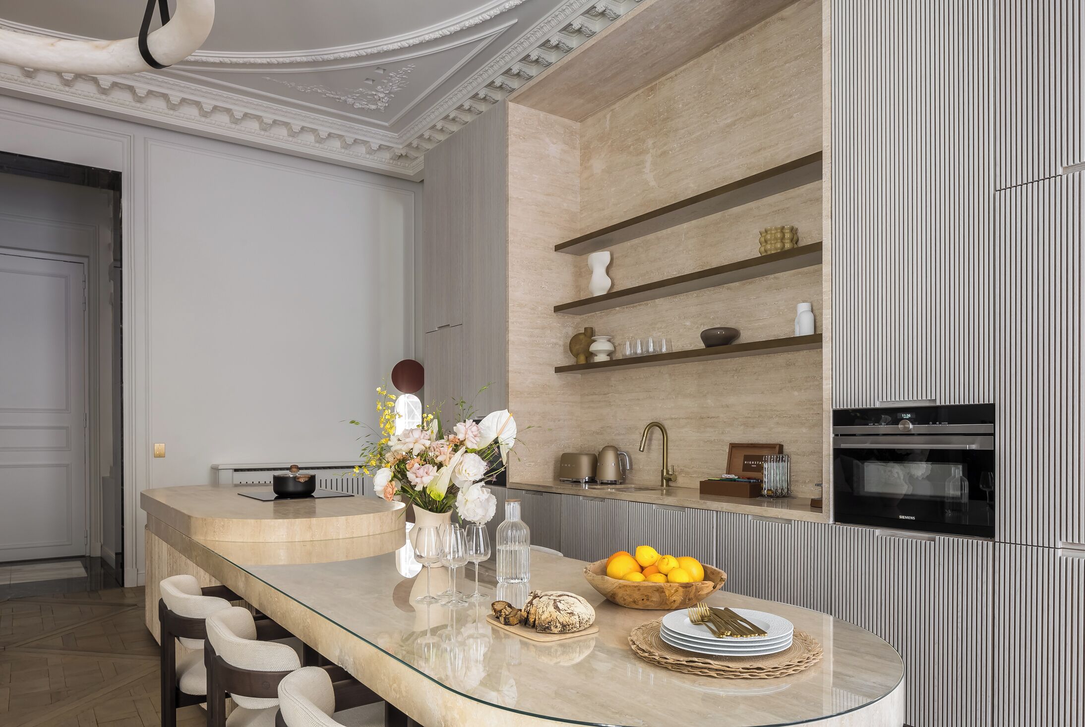 A modern kitchen with a curved island, built-in shelves, and a large oven.