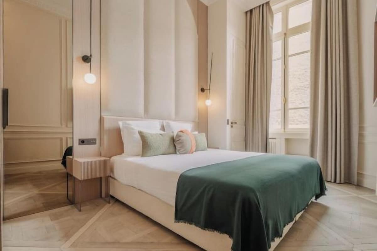 A modern bedroom with a large bed, bedside lamps, and a view of the outdoors through a window.