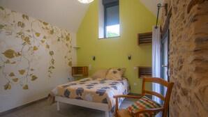 A bedroom with a bed, a chair, a window, and a wall with a leaf pattern.