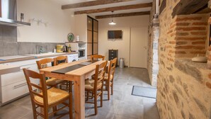 A modern kitchen with wooden beams, a dining area with a wooden table and chairs, and a stone wall.