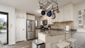 Una cocina moderna con armarios blancos, electrodomésticos de acero inoxidable, una encimera de granito y ollas colgantes.