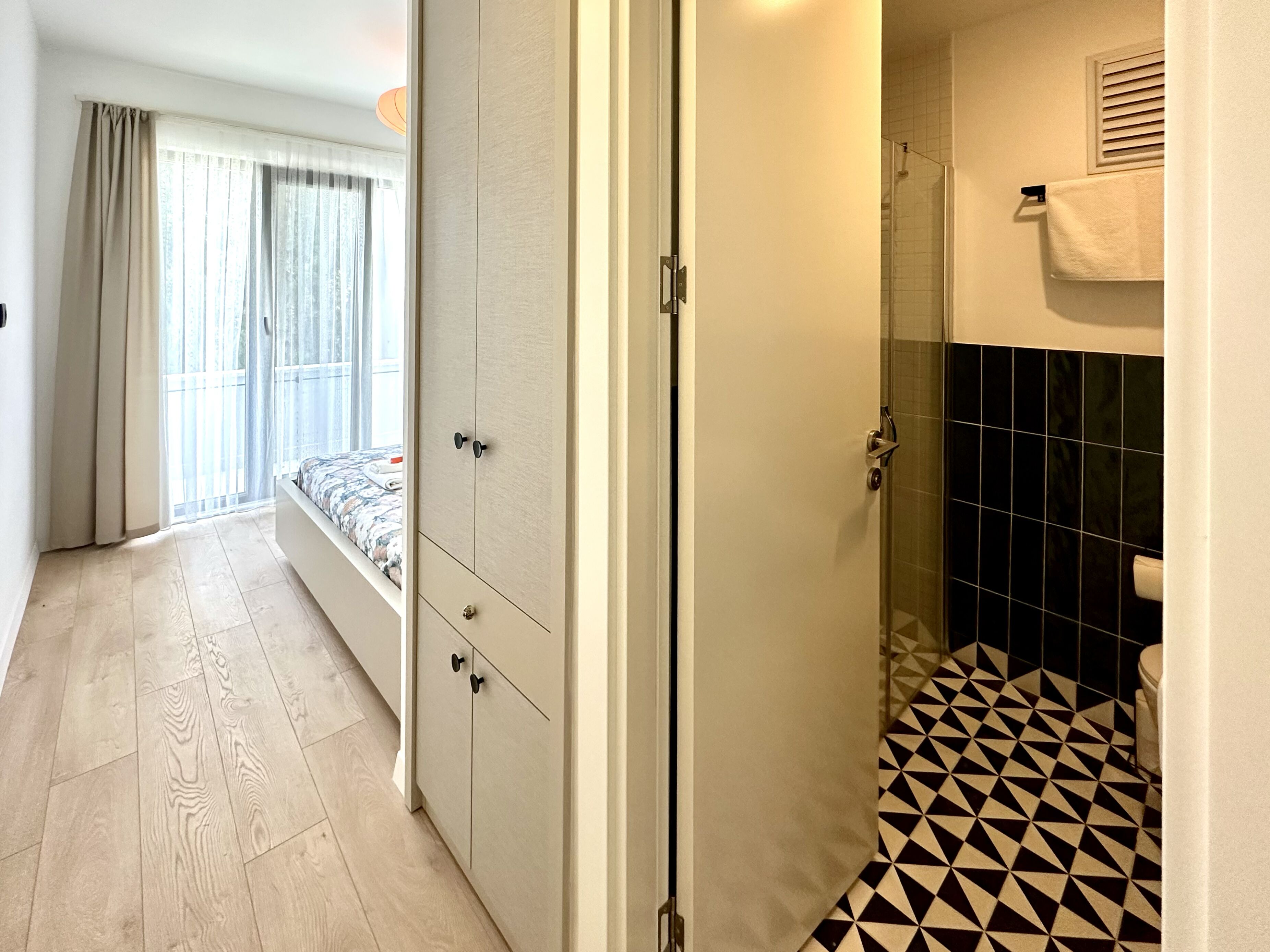 A hotel room with a bed, wardrobe, and a bathroom with a geometric tile floor.