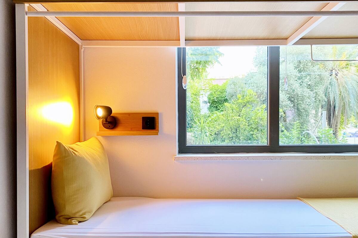 A bunk bed with a window, a bedside lamp, and a small shelf.
