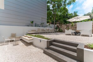 Une terrasse extérieure moderne, dotée d’un espace salon, de quelques marches et d’une petite table avec un parasol.