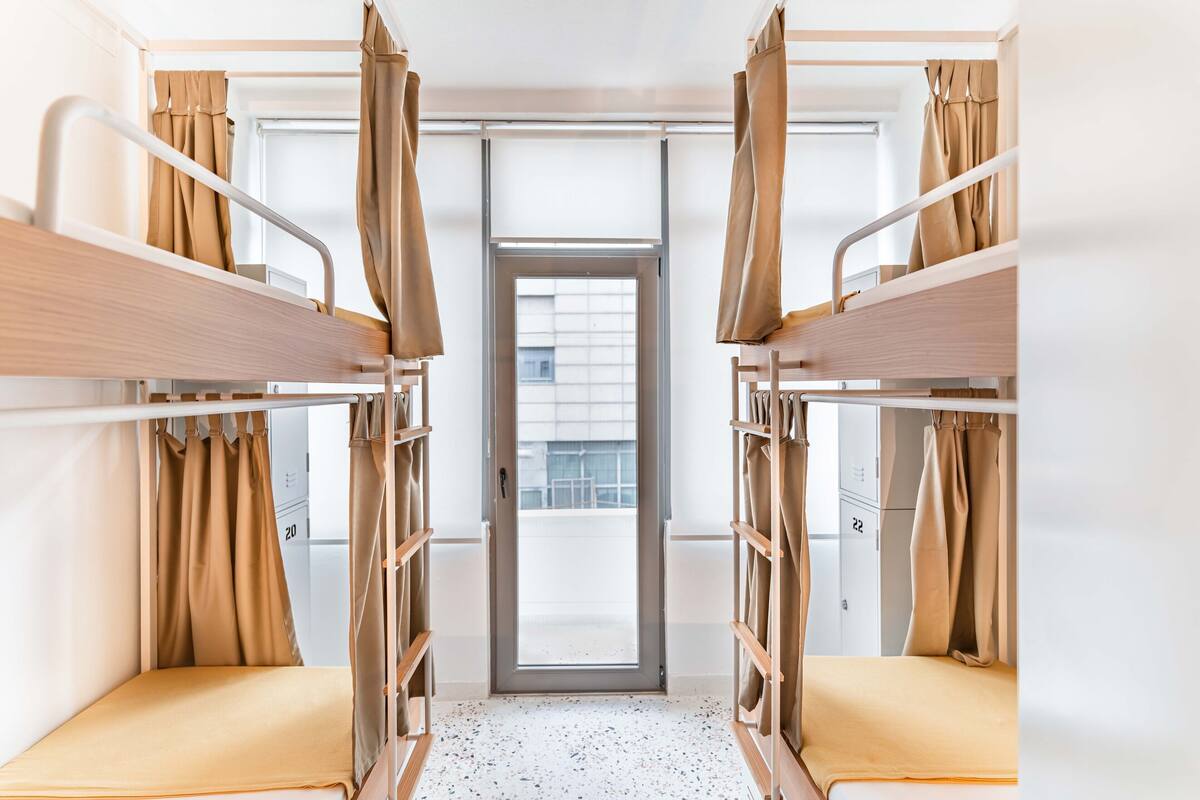A dormitory room with bunk beds, a door, and a window.