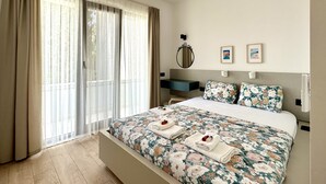 A bedroom with a large bed, a bedside table, a mirror, and a view of the outdoors through the window.