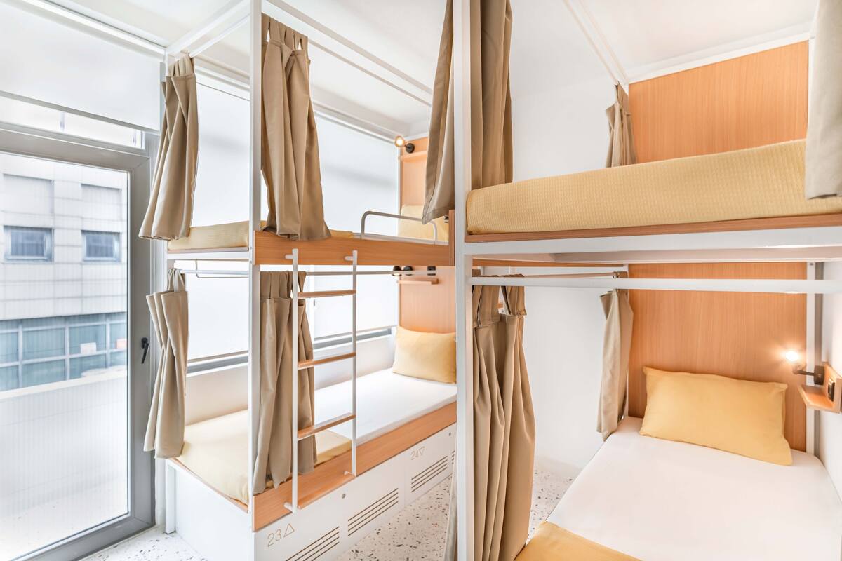A bunk bed room with curtains, a window, and a small bedside table.