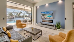 Un soggiorno moderno con una grande TV, posti a sedere comodi e vista sulla piscina e l'area esterna.