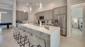 Una cucina moderna con isola centrale, sgabelli da bar, elettrodomestici in acciaio inossidabile e illuminazione a sospensione.