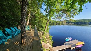 A wooden deck with blue chairs, a wooden staircase, and a dock with colorful kayaks. - Rustic-Luxury Waterfront Cottage Getaway on Kennisis Lake Stunning Elevated View (Haliburton)
