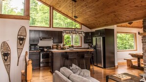 A modern kitchen with dark cabinets, a central island, and a large window. - Rustic-Luxury Waterfront Cottage Getaway on Kennisis Lake Stunning Elevated View (Haliburton)