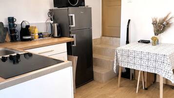 A compact kitchen with a microwave, refrigerator, and stove. There is a dining table with a floral tablecloth and a vase with dried flowers.